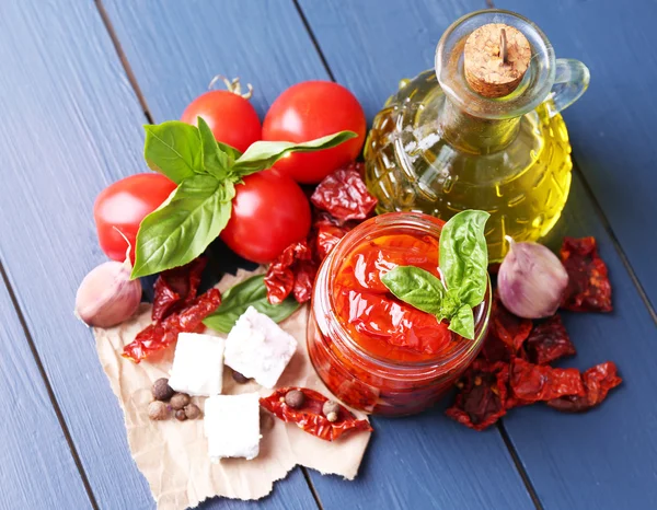 Tomates secos ao sol em jarra de vidro, azeite em garrafa de vidro e queijo feta em fundo de madeira de cor — Fotografia de Stock