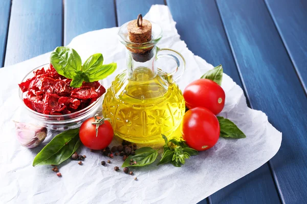 Sun dried tomatoes in glass jar, olive oil in glass bottle, basil leaves on color wooden background — Stock Photo, Image