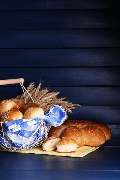 Pães saborosos com gergelim na cesta, na cor de fundo de madeira — Fotografia de Stock