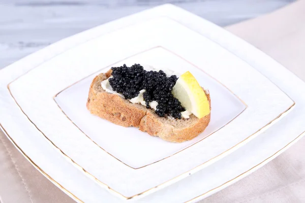 Tranche de pain au beurre, caviar noir et citron sur assiette sur serviette sur fond bois gris — Photo