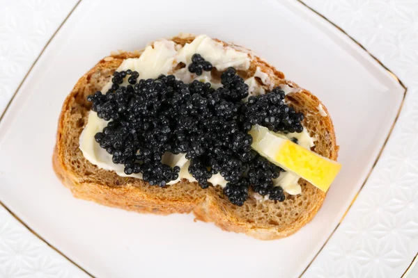 Шматочок хліба з маслом, чорною ікрою та лимоном на тарілці крупним планом — стокове фото