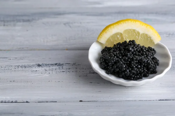 Caviale nero con limone su piatto su fondo grigio in legno — Foto Stock