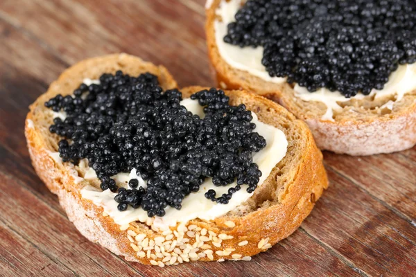 Skivor bröd med smör och svart kaviar på trä bakgrund — Stockfoto