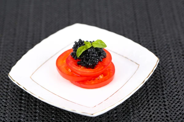 Fette di pomodoro con caviale nero su piatto su fondo tessuto scuro — Foto Stock