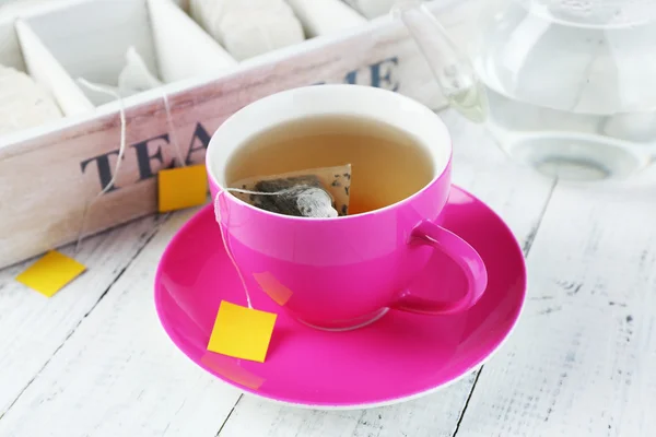 Taza con té, tetera y bolsitas de té en primer plano de mesa de madera — Foto de Stock