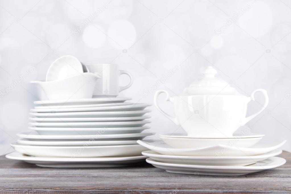 White crockery and kitchen utensils, on wooden table, on light background