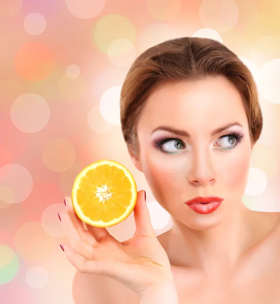 Beautiful young woman with bright make-up holding orange on bright background — Stock Photo, Image