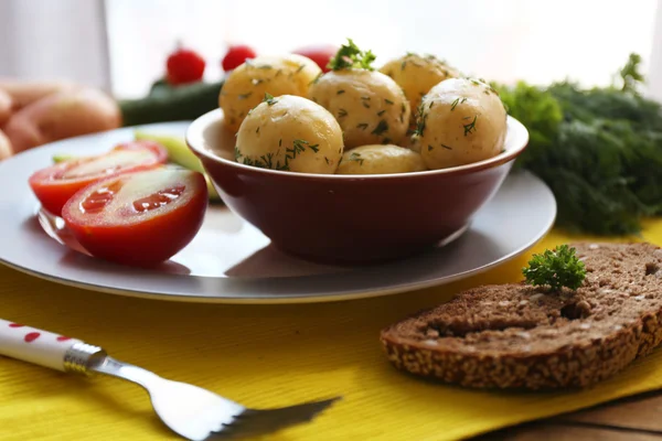 Jonge gekookte aardappelen met groenten op tafel op achtergrond van venster — Stockfoto