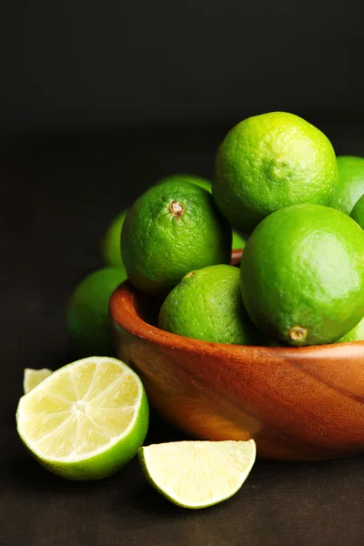 Frische saftige Limetten in Holzschale, auf dunklem Hintergrund — Stockfoto