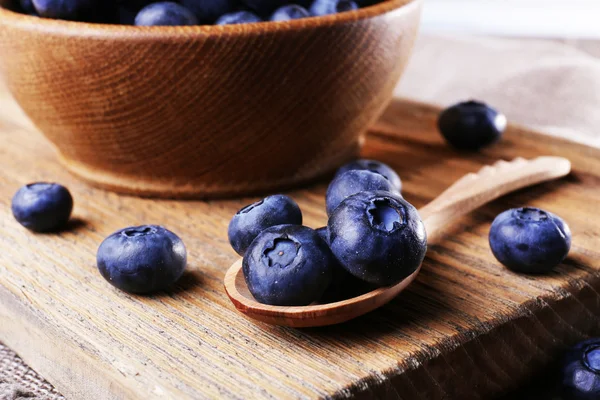 Wooden bowl of blueberries on cutting board on wooden background — Stock Photo, Image