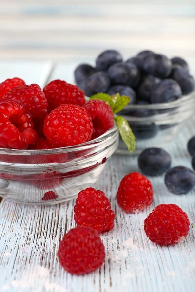 Glass bowls of raspberries and blueberries on wooden table on light background — Stock Photo, Image