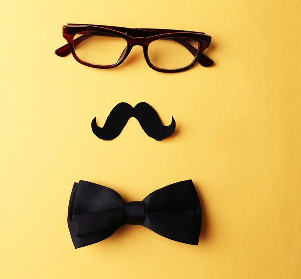 Glasses, mustache and bow tie forming man face on yellow background — Stock Photo, Image