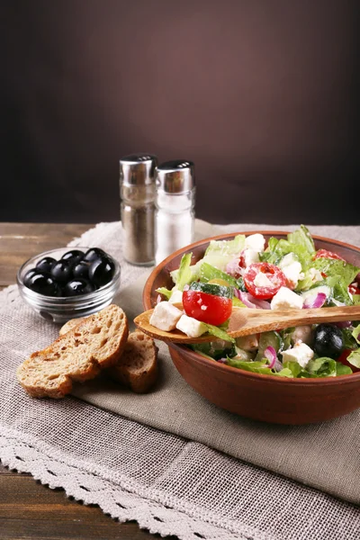 Bowl of Greek salad served on napkin on wooden table on dark background — Stock Photo, Image