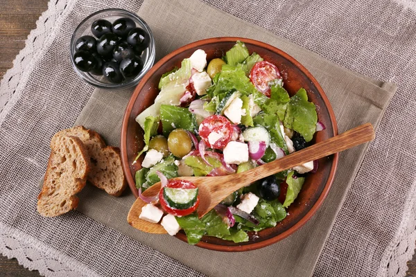 Bowl of Greek salad served on napkin on wooden background closeup — Stock Photo, Image