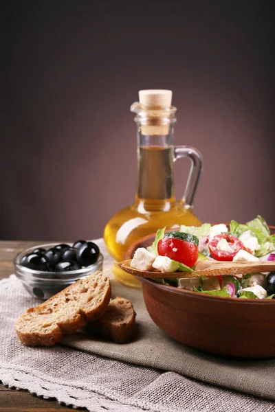 Bowl of Greek salad served with olive oil on sacking napkin on wooden table on dark background — Stock Photo, Image