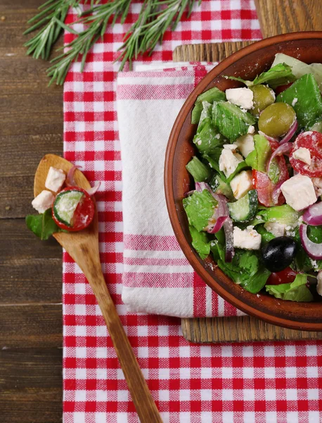 Kom van Griekse salade geserveerd op snijden bestuur servet op houten tafel op donkere achtergrond — Stockfoto