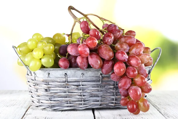 Ramos de uva madura en canasta de mimbre sobre mesa de madera sobre fondo natural —  Fotos de Stock