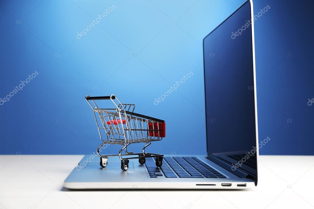 Shopping cart on laptop on table, on blue background