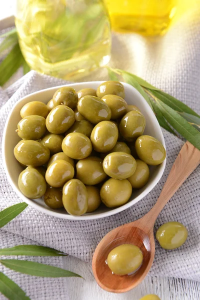 Zielone oliwki w misce z liści na stół szczegół — Zdjęcie stockowe