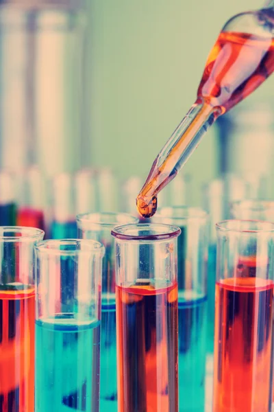 Pipeta de laboratorio con gota de líquido de color sobre tubos de ensayo de vidrio, primer plano — Foto de Stock