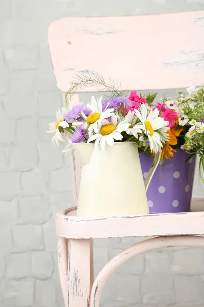 Bouquet of colorful flowers in decorative buckets, on chair, on light wall background — Stock Photo, Image