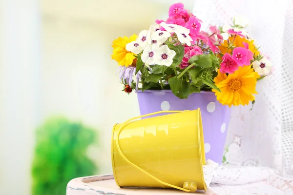 Strauß bunter Blumen im dekorativen Eimer, auf Stuhl, auf hellem Hintergrund — Stockfoto