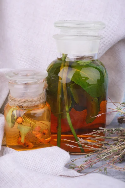 Bottles of herbal tincture and dried herbs on a napkin on wooden background in front of curtain — Stock Photo, Image