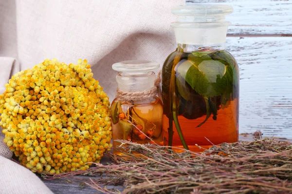 Bottles of herbal tincture and dried herbs on a napkin on wooden background in front of curtain — Stock Photo, Image