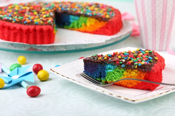 Deliziosa torta arcobaleno su piatto e tazza con caffè, sul tavolo, su sfondo chiaro — Foto Stock