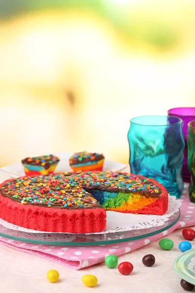Delicioso pastel de arco iris en la mesa, sobre un fondo brillante — Foto de Stock