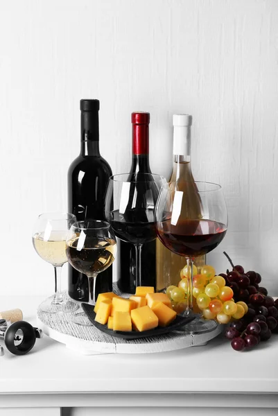 Bottles and glasses of wine, cheese and ripe grapes on table in room — Stock Photo, Image