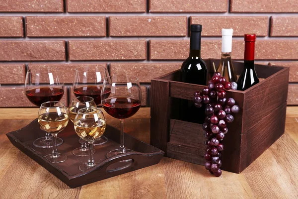 Flaschen und Gläser mit Wein und reifen Trauben auf dem Tisch vor Backsteinmauer Hintergrund — Stockfoto