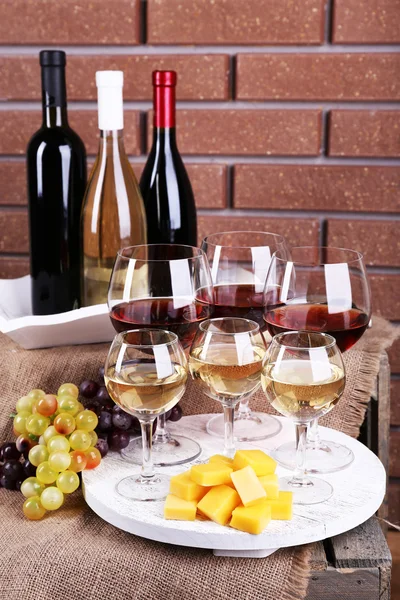 Botellas y vasos de vino, queso y uvas maduras en la mesa sobre fondo de pared de ladrillo — Foto de Stock