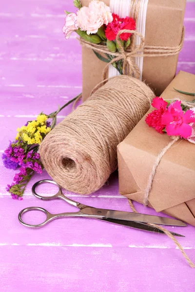 Beautiful gifts with flowers and decorative rope, on old wooden background — Stock Photo, Image