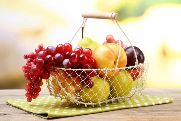 Surtido de frutas jugosas en canasta de mimbre sobre mesa, sobre fondo brillante — Foto de Stock