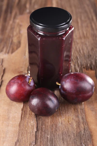 Confiture de prunes savoureuse en pot et prunes sur table en bois close-up — Photo