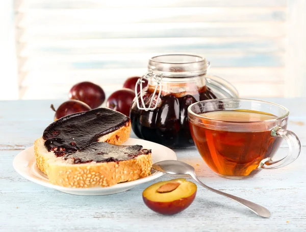 Brot mit Pflaumenmarmelade und Tee auf Holztisch — Stockfoto