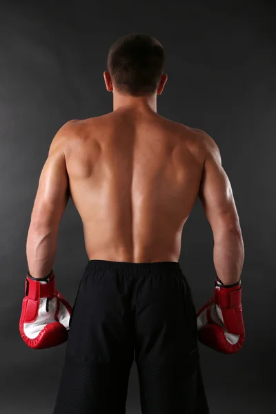 Beau jeune sportif musclé avec des gants de boxe sur fond sombre — Photo