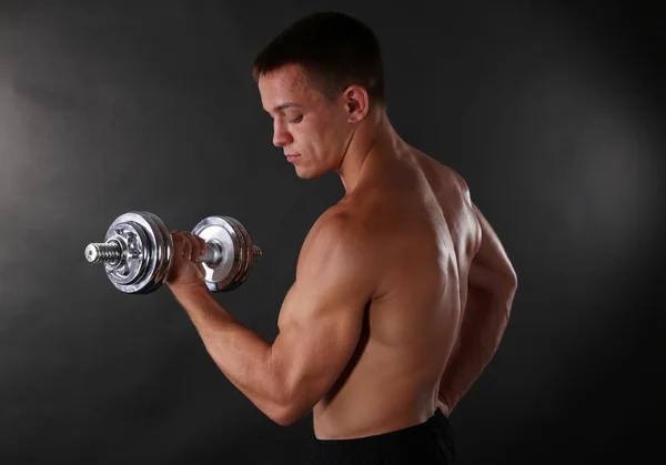 Bonito jovem desportista muscular executar exercício com halteres no fundo escuro — Fotografia de Stock