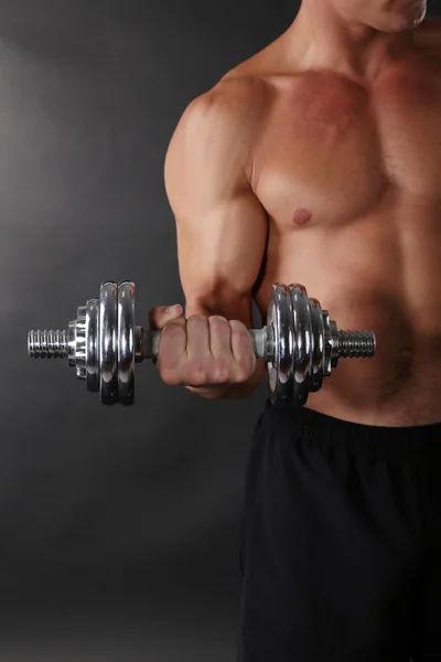 Muscle young sportsman execute exercise with dumbbell on dark background — Stock Photo, Image