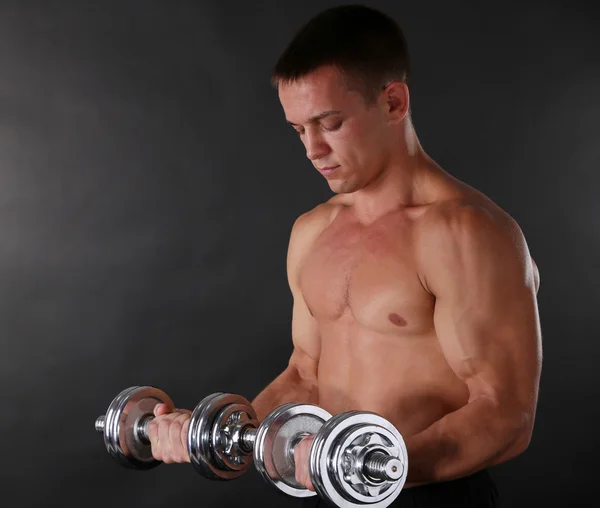 Handsome young muscular sportsman execute exercise with dumbbells on dark background — Stock Photo, Image