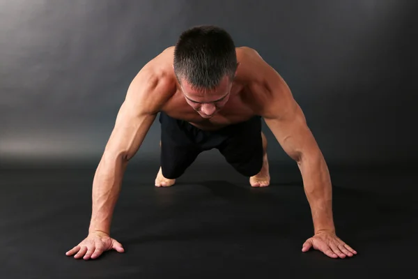 Bonito jovem desportista muscular executar exercício em fundo escuro — Fotografia de Stock