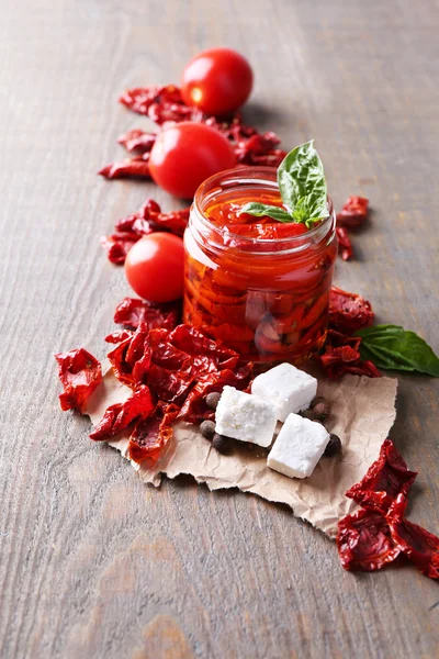 Sun dried tomatoes in glass jar, basil leaves and feta cheese on color wooden background — Stock Photo, Image