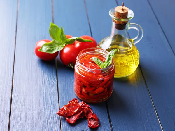 Sun dried tomatoes in glass jar on color wooden background — Stock Photo, Image