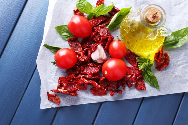 Sun dried tomatoes in glass jar, olive oil in glass bottle, basil leaves on color wooden background — Stock Photo, Image