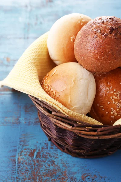 Tasty buns with sesame in wicker basket, on color wooden background — Stock Photo, Image