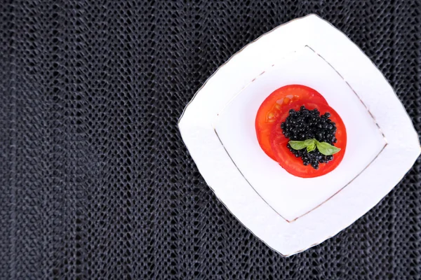 Slices of tomato with black caviar on plate on dark fabric background — Stock Photo, Image