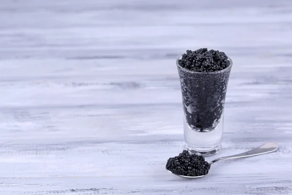 Vidrio y cuchara de caviar negro sobre fondo de madera gris — Foto de Stock