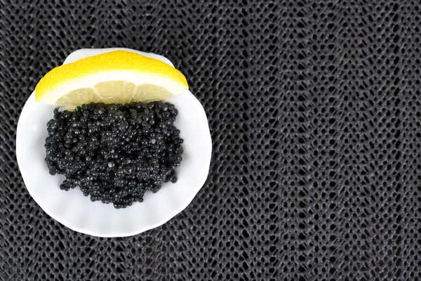 Caviale nero con limone su piatto su sfondo tessuto scuro — Foto Stock