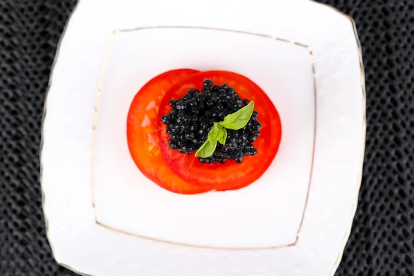 Plastry pomidora z czarnym kawiorem na tabliczce na tle ciemnej tkaniny — Zdjęcie stockowe